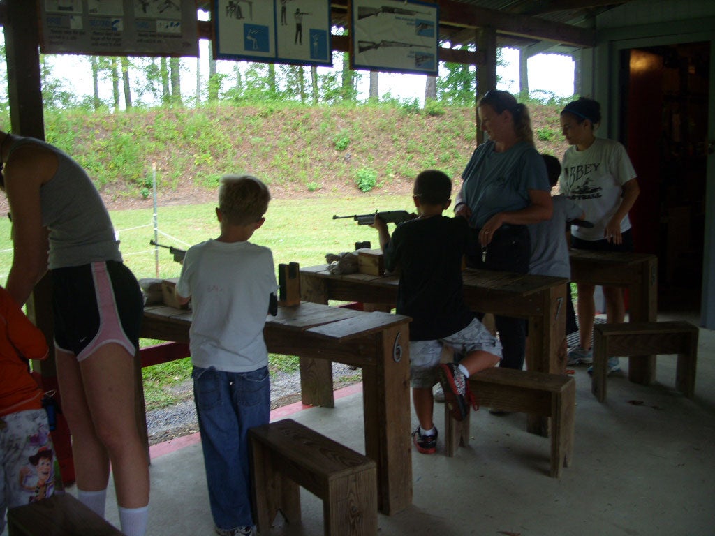 Group of campers standing at a line of gun rests pointing long BB guns down a range.